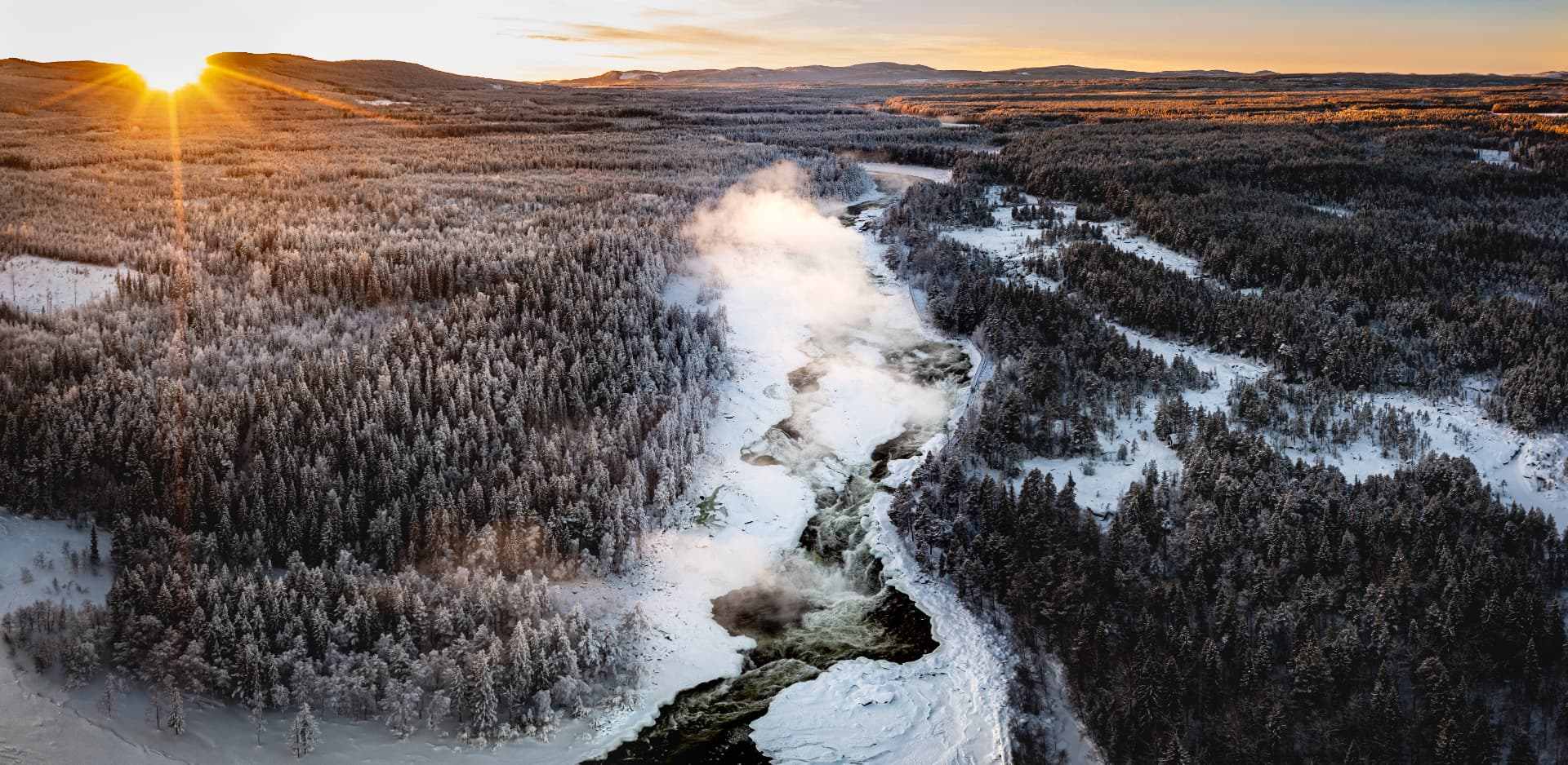 Aerial view of a snow-covered forest and river at sunset