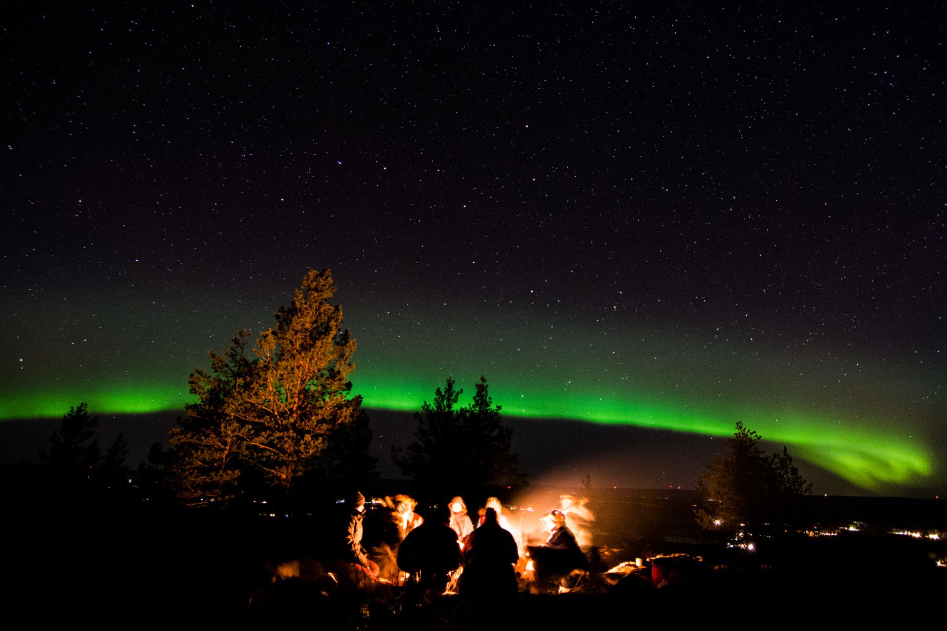 Guests gathered around a fire beneath the northern lights in the Arctic